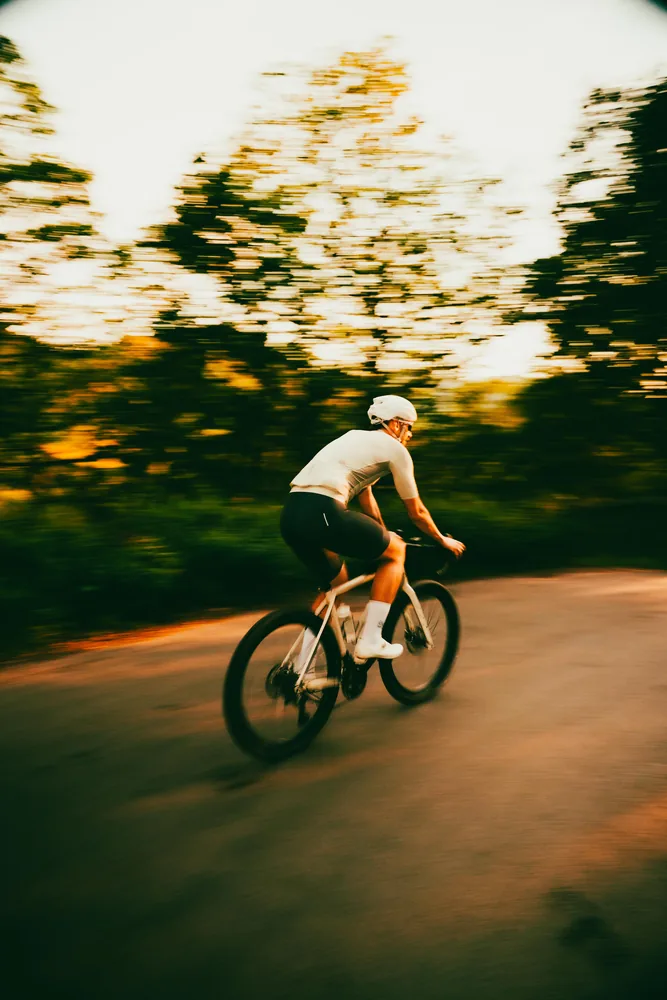 A cyclist descending a gravel trail at golden hour, motion blurred against the trees.