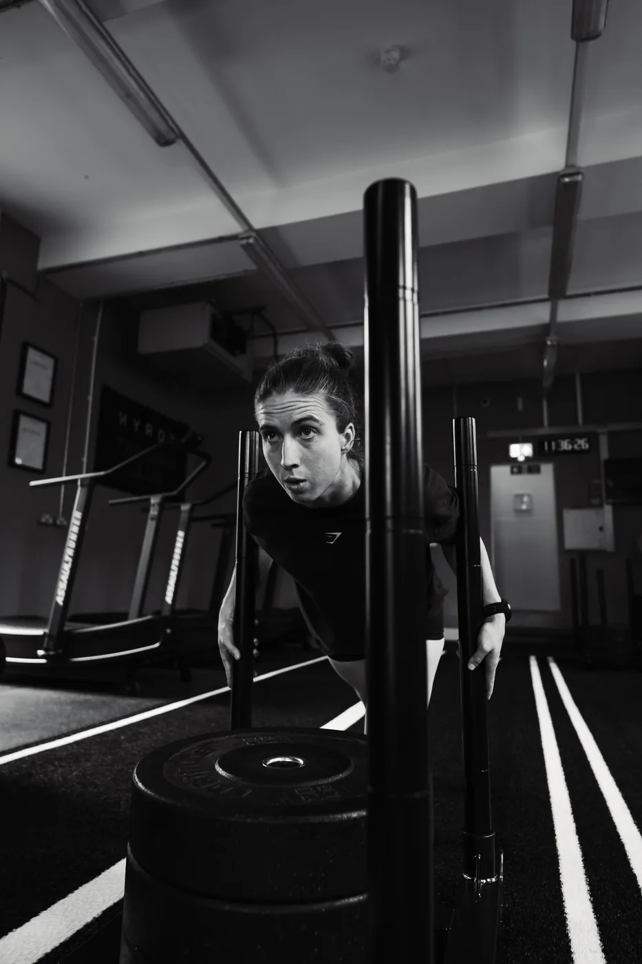 An athlete pushing a weighted sled straight toward the camera on a gym track, in high contrast black and white.